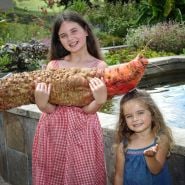 A couple of adorable girls smilling while holding a  Mammoth Red Mangel Beet in the garden at Baker Creek.