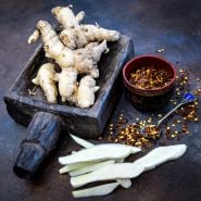 Sliced and whole Mango Ginger roots with chili flakes and props from India on dark background.
