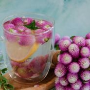 Atomic Purple Gomphrena tea with a bouquet of blooms rests on a wooden background.