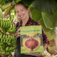 Deb smiles as she shows off the Baker Creek Handy Tote Bag by a banana tree.