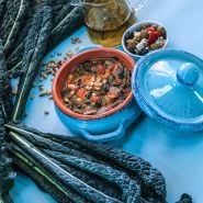 Nero di Toscana Kale soup with condiments on a blue background with fresh leaves.