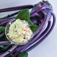 Kohlrabi salad in a glass bowl on top of a bunch of Early Purple Vienna Kohlrabi.