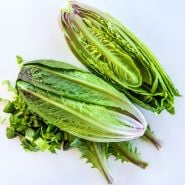 One halved and one whole head each of Brown Goldring Lettuce with chopped leaves on a white background.