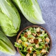 Three Crisp Mint Lettuce heads and a bowl of salad on a stone background.