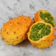 Two Kiwano African horned jelly melons, one sliced in half, the other whole on a marble background.