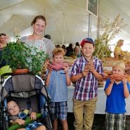 A mom and her kiddos posing with some plants and sweet potatoes at the Baker Creek Fall Harvest Festival.
