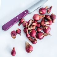 Red Catawissa Walking Onion Bulbils with a purple handled knife on a light background.