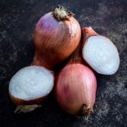 Cut and whole Red Catawissa Walking Onion Bulbs on a dark brown background.