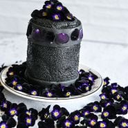 A black fondant cake surrounded by Bowles Black Violas on a light background.