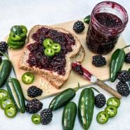 An overhead view of Apache Blackberry and jalapeno jam on toast with a jam knife and jar.