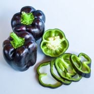 Two Purple Beauty Peppers next to slices on a light background. 