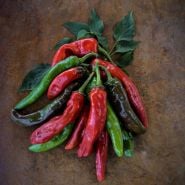 Red, green, and greenish-brown Txorixero Peppers and leaves on a wooden background.