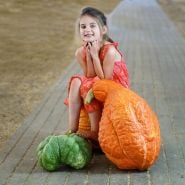 A girl smiles while sitting on a Boston Marrow Squash at the Sonoma County Fairgrounds.