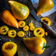 Chopped and whole Orange Lesya Sweet Peppers with a knife on a wooden cutting board.