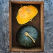 One cut and one whole Buttercup Winter Squash in wooden box on metal background.