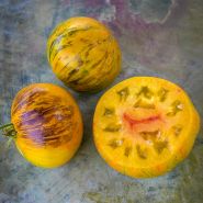 Two whole Alice's Dream Tomatoes with a tomato cut in half to show the yellow and red meat inside.