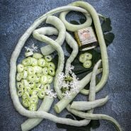 Whole and cut Indian Snake Bean with vintage curry powder can on a dark background.