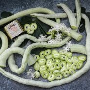 A closer view of whole and sliced Indian Snake Beans with fllowers all intertwined together.