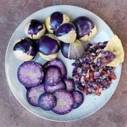 An overhead view of a plate of sliced and whole Purple Tomatillos with salsa and a corn chip.