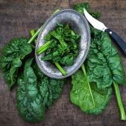 Giant Noble Spinach leaves with a knife on a wood board.   