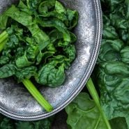 A close-up of Giant Noble Spinach leaves in a silver bowl surrounded by leaves.
