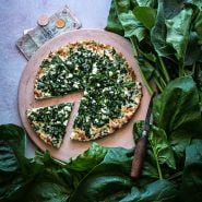 Gigante d' Inverno Spinach leaves surrounding a spinach and feta pizza on a pizza stone with Italian money.
