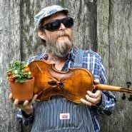 A musician poses with amini-tomato and his fiddle with a "fiddler spider" at the Baker Creek Spring Planting Festival.