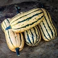 Four Honey Boat Delicata Winter Squash arranged n a wooden cutting board.