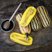 Whole and cut open Honey Boat Delicata Winter Squash on a wooden cutting board with honey.