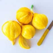 Lemon Summer Squash with a wedge cut and a yellow handled knife against a white background.