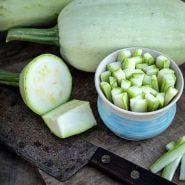 Whole and chopped Odessa Summer Squash on a wooden cutting board.