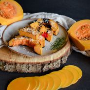 Roasted Butternut-Orange Winter Squash on a plate surrounded by cut squash on a dark background.