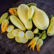 Cut and whole Early Prolific Straightneck Summer Squash arranged on wooden with blooms.