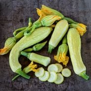 Cut and whole Rugosa Friulana Summer Squash arranged on wooden background with blooms.