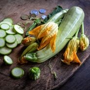Long White of Palermo Zucchini Summer Squash with slices and blooms on wooden cutting board.