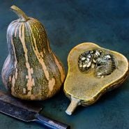 A whole and a halved Ayote Green Flesh Winter Squash on a dark jade background with a knife.
