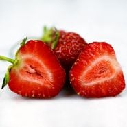 A close-up macro view of a sliced Old North Sea Strawberry with whole berries in the background.