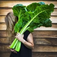 A woman holding Fordhook Giant Swiss Chard leaves over her shoulder. Image by Lucy Hutchins.