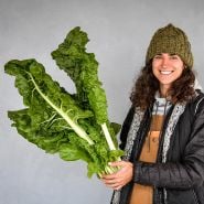 Baker Creek employee smilingand holding a head of Fordhook Giant Swiss Chard. 