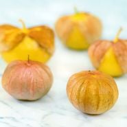 Five Amarylla Tomatillo fruit with husks on a white marble background.