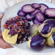 Hand holding a plate of whole, sliced Purple Tomatillos with a side of purple salsa.