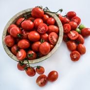 A bowl full of  A Grappoli D'Inverno Tomatoes surrouunded by cut tomatoes on a white background.
