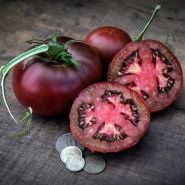 Cut and whole Black from Tula Tomatoes with coins on wood background.