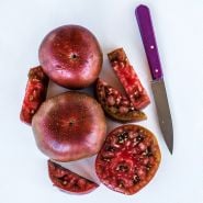 Cut and whole Black Krim Tomatoes arranged with a purple handled knife on white background.