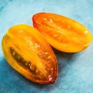 A close-up of a cut Tiger Blush Tomato on light bluebackground.