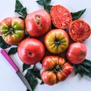 Cut and whole Brandywine Tomatoes arranged on white background with a pink handled knife.