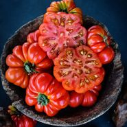 Cut and whole Burmese Sour Tomatoes in a rustic wooden bowl on a dark jade background.
