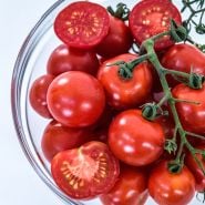 Close-up view of Chadwick Cherry or Camp Joy Tomatoes in a glass bowl on a white background.