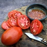 Sliced and juiced Comstock Sauce and Slice Tomato on a wood cutting board with a wood handled knife.