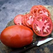Close-up of a whole Comstock Sauce and Slice Tomato with slices and knife on wood cutting board.